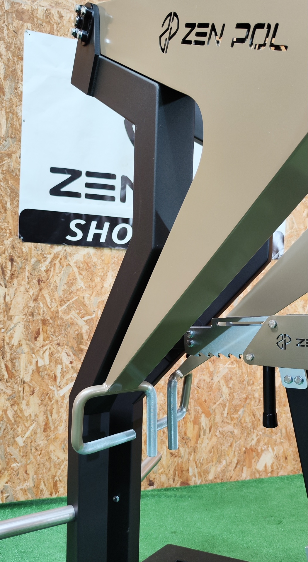 Equipamento de treino metálico preto e bege com ganchos, parede de madeira e placa 'ZEN POL'.