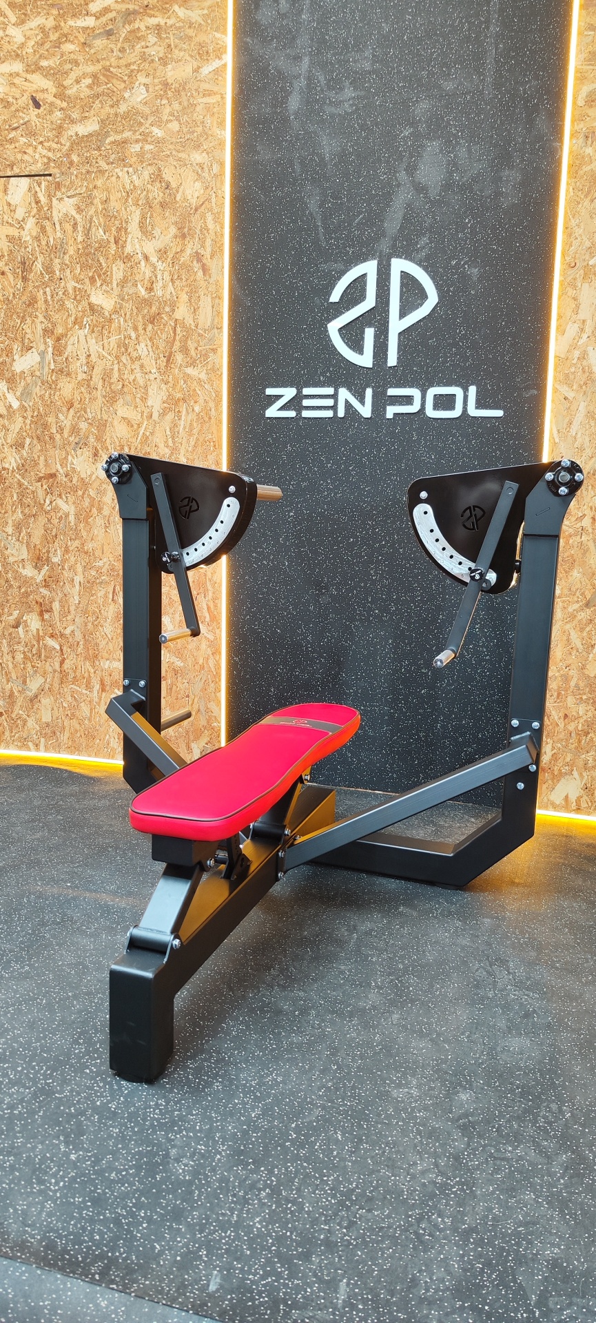 Banco de treino preto com assento vermelho junto a parede com logotipo ZEN POL