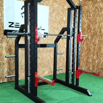 Power rack preto com detalhes vermelhos e barra cromada sobre piso verde e parede de madeira.