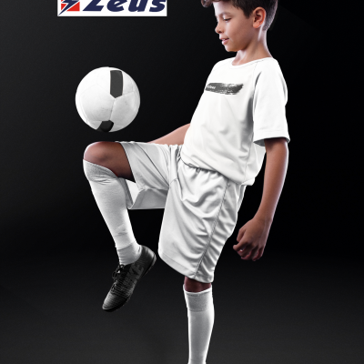 Menino em fato de treino desportivo branco com bola de futebol e logótipo Zeus