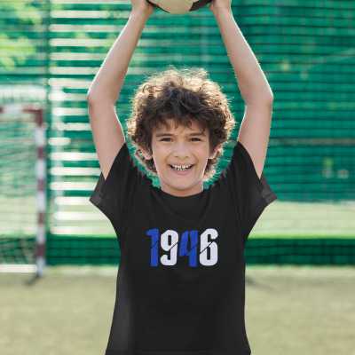 Camisola preta com 1946 estampado, criança segurando bola de futebol, campo de futebol ao fundo