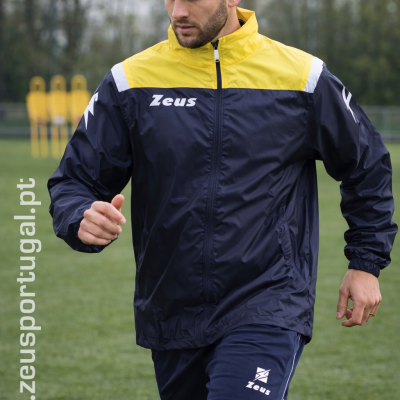 Homem a jogar futebol com roupa desportiva azul e amarela Zeus em campo de relva
