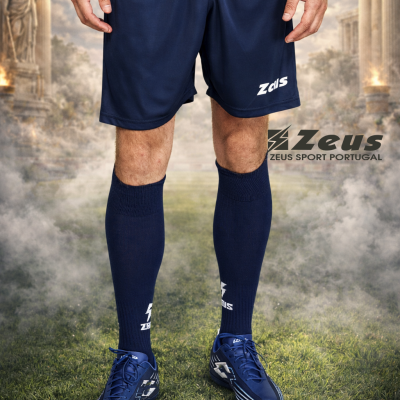Roupa desportiva azul com logótipo Zeus em cenário de relvado e ruínas clássicas.