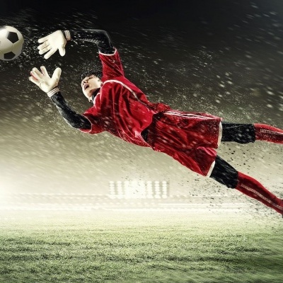 Guarda-redes de futebol a saltar para agarrar uma bola num campo de futebol à noite