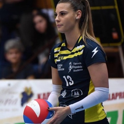 Jogadora de voleibol com uniforme azul escuro e amarelo segurando bola de voleibol nas cores vermelho, branco e azul