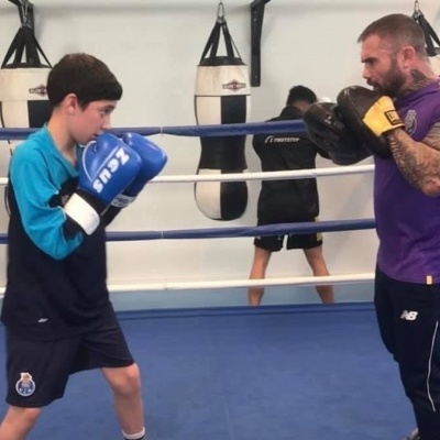 Dois homens a treinar boxe no ringue, um com luvas azuis e outro com luvas amarelas.