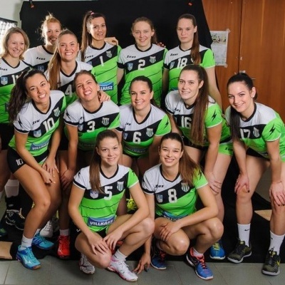 Equipa feminina de voleibol com uniformes verdes, pretos e brancos num espaço interior