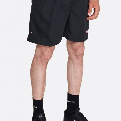 Homem usando calções desportivos pretos com detalhes vermelhos e logótipos, meias e ténis pretos em fundo branco