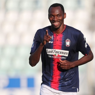Jogador de futebol com camisola azul escura e risca vermelha em campo.