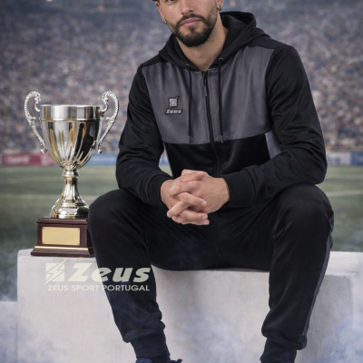 Homem com roupa desportiva preta e cinza sentado ao lado de troféu prateado