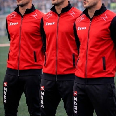 Três homens de casacos e calças desportivas vermelhas e pretas com logo Zeus em campo