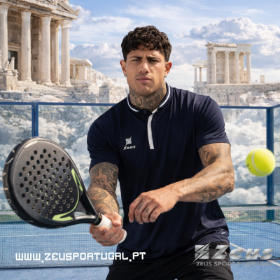 Homem a jogar padel com camisa azul escuro e raquete preta num campo de padel com ruínas antigas ao fundo