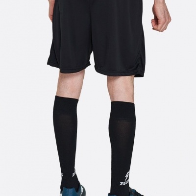 Pessoa de costas a usar calções pretos, meias negras compridas com logo ZETT e sapatos desportivos azuis.