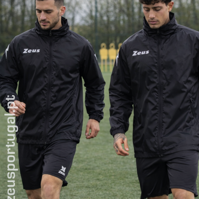 Dois homens com fato de treino preto da marca Zeus em campo de futebol com bola preta e branca