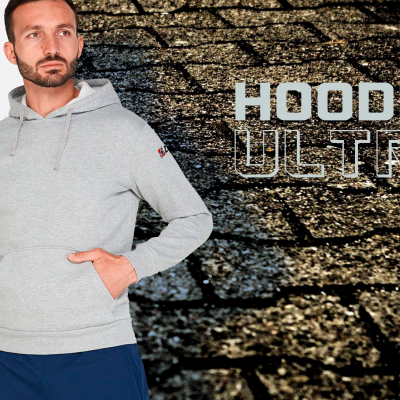 Homem com hoodie cinzento e calças azuis com fundo de parede em pedra escura e texto hoodie ultra