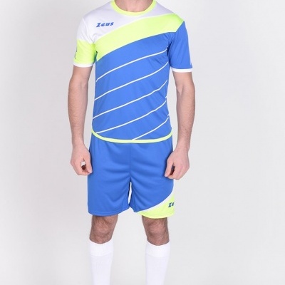 Homem com fato de treino azul com amarelo fluorescente e branco, t-shirt com riscas e texto Zeus, calções azuis, meias brancas e sapatilhas pretas.