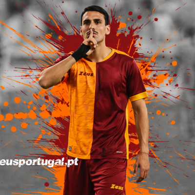 Jogador de futebol com camisola bicolor vermelho grená e laranja e calções com marca Zeus