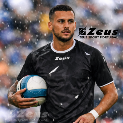 Jogador de futebol a usar camisola preta Zeus e segurando uma bola azul e branca na chuva