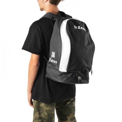Mochila preta e branca da marca Zeus usada por pessoa com t-shirt preta e calças camufladas