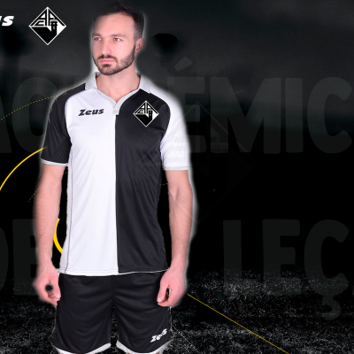 Homem com fato desportivo bicolor preto e branco com logótipos Zeus e escudo numa camisola e calções pretos.