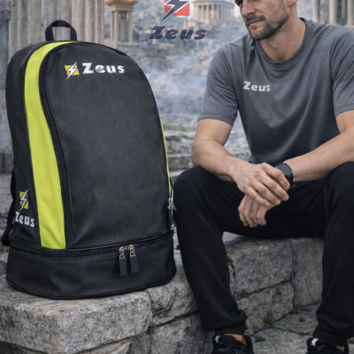 Mochila preta com laterais amarelas e logótipo Zeus colocada sobre pedra com homem sentado ao lado