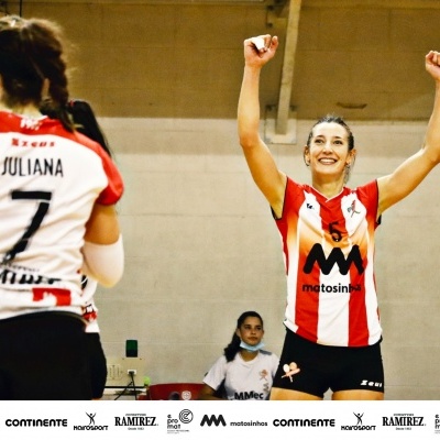 Duas jogadoras de voleibol em uniforme vermelho, branco e preto num ginásio.
