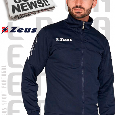 Homem com casaco desportivo azul escuro com logo 'Zeus' e texto 'Zeus Sport Portugal' no fundo e jornal 'DAILY NEWS GOOD NEWS!!'