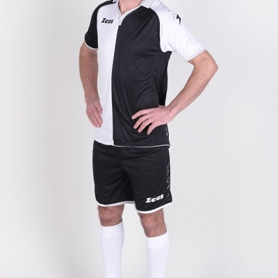 Homem com fato de futebol preto e branco, meias brancas e sapatilhas pretas em fundo branco.