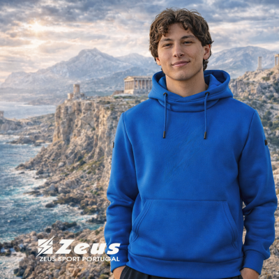 Homem jovem com sweatshirt azul à beira-mar rochoso com ruínas antigas ao fundo