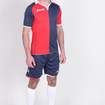 Homem com fato de futebol vermelho e azul, calções azuis, meias brancas e sapatilhas pretas