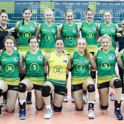 Equipa feminina de voleibol em uniformes verdes e amarelos posando no ginásio.