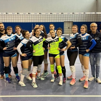 Equipa de voleibol numa quadra desportiva em uniformes azuis, brancos e verdes.