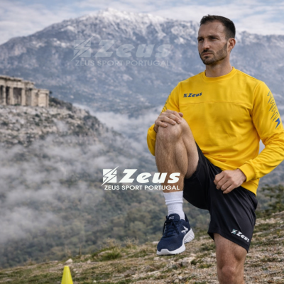 Homem com roupa desportiva amarela e preta em cenário montanhoso com ruínas ao fundo