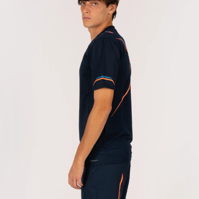 Homem de pé com roupa desportiva azul escuro com detalhes laranja e azul em fundo branco