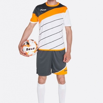 Homem vestido com fato de treino colorido e a segurar uma bola de futebol.