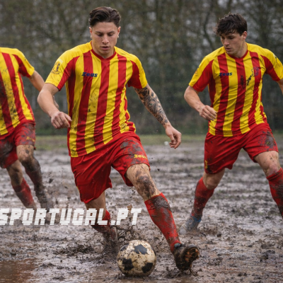Jogadores de futebol com camisolas amarelas e vermelhas a jogar num campo lamacento
