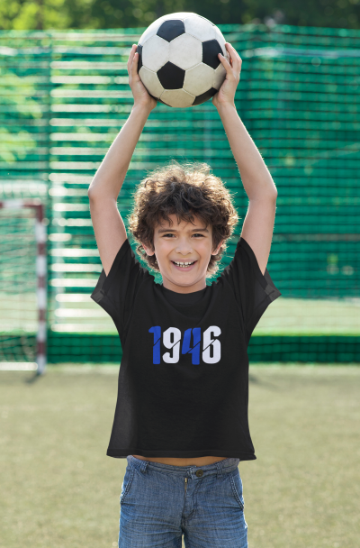 Camisola preta com 1946 estampado, criança segurando bola de futebol, campo de futebol ao fundo