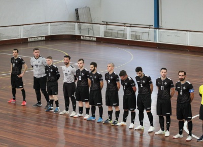 Dez jogadores de futsal em linha numa quadra coberta com piso de madeira.