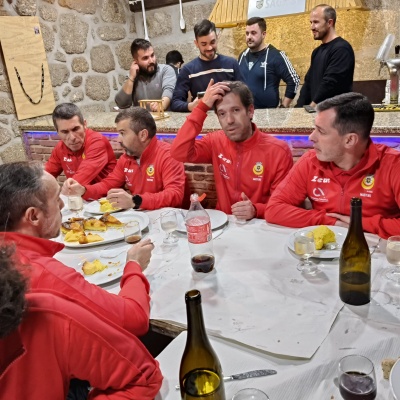 Homens com fato de treino vermelho a comer e beber numa mesa com toalha branca