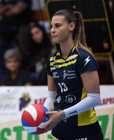 Jogadora de voleibol com uniforme azul escuro e amarelo segurando bola de voleibol nas cores vermelho, branco e azul