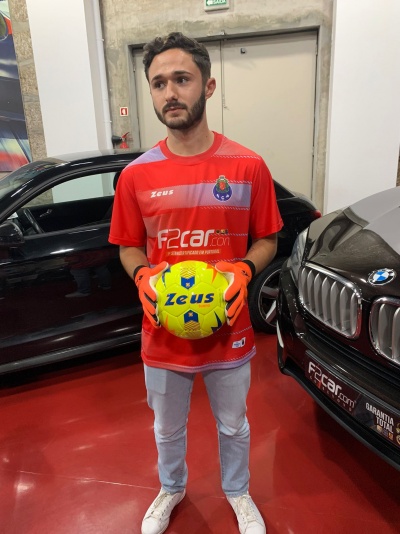 Homem com camisola de futebol vermelha segurando bola amarela Zeus na garagem entre carros BMW e Audi pretos