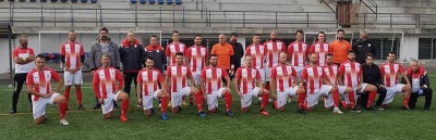 Equipa de futebol com uniformes listrados vermelhos e brancos em campo de relvado com arquibancada