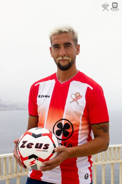 Homem vestindo camisa desportiva vermelha, branca e laranja segurando uma bola de futebol vermelho e branco com logótipo Zeus.