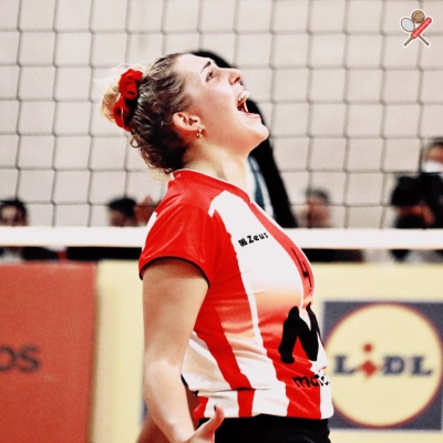 Jogadora de voleibol com uniforme vermelho e branco perto da rede e cartaz do Lidl ao fundo