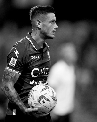 Jogador de futebol com equipamento escuro segurando bola branca com padrões