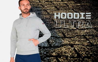 Homem com hoodie cinzento e calças azuis com fundo de parede em pedra escura e texto hoodie ultra