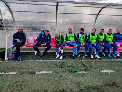 Jogadores e técnicos sentados no banco de reservas de futebol sob abrigo transparente no campo artificial