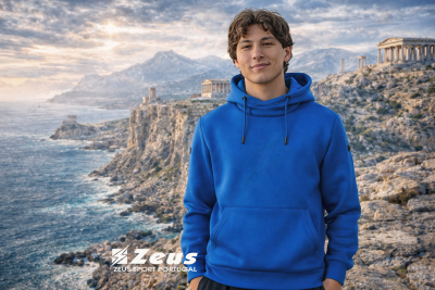 Homem jovem com sweatshirt azul à beira-mar rochoso com ruínas antigas ao fundo