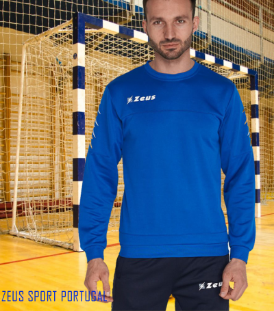 Homem de azul e preto com logos Zeus em quadra desportiva com baliza atrás