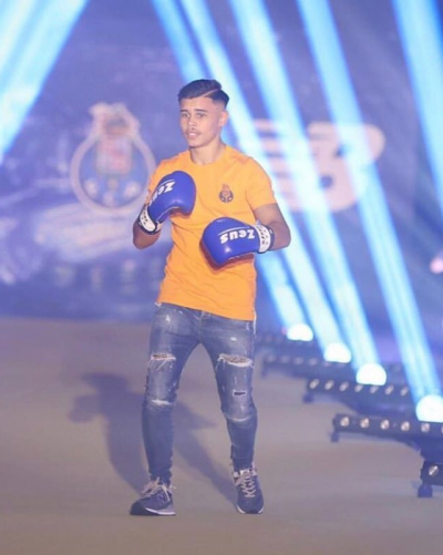 Homem com t-shirt amarela, calças de ganga rasgadas e luvas de boxe azuis em palco iluminado.